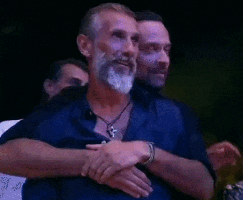 two men are hugging each other with their eyes closed in a dark room .