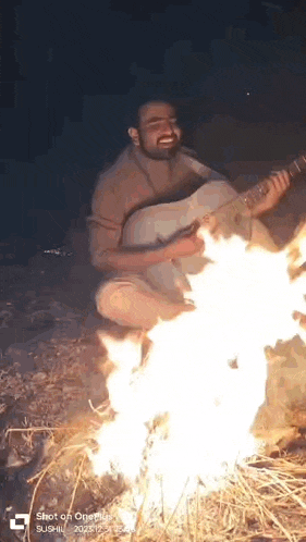 a man is sitting on the ground playing a guitar in front of a fire .