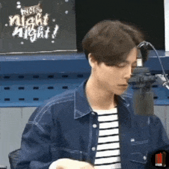 a man in a striped shirt is standing in front of a microphone in a room .