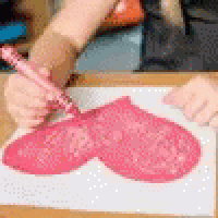 a person is drawing a pink heart on a piece of paper .