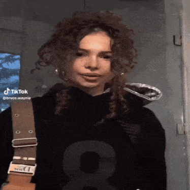 a girl with curly hair is wearing a black hoodie with the number 8 on the front