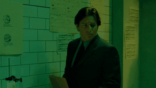 a man in a suit and tie is standing in a dark room with a green light behind him .