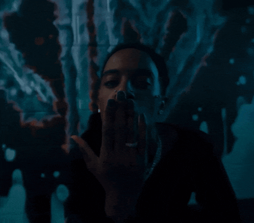 a man smoking a cigarette in a dark room with a blue background