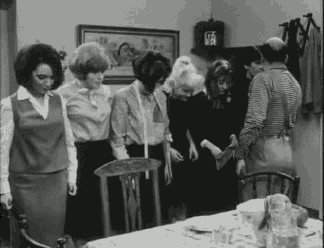 a black and white photo of a group of people standing around a table with the letter g on the wall