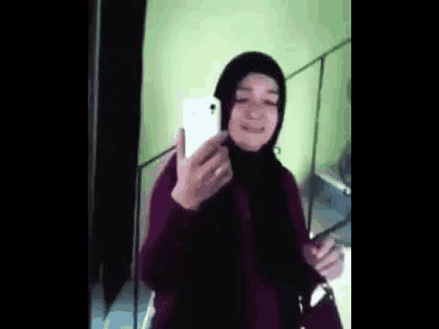 a woman wearing a hijab is taking a selfie with her cell phone .