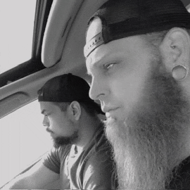 a man with a beard wearing a hat is sitting next to another man in a car