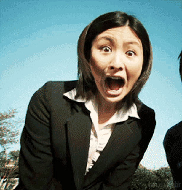 a woman in a suit is making a surprised face with her mouth wide open