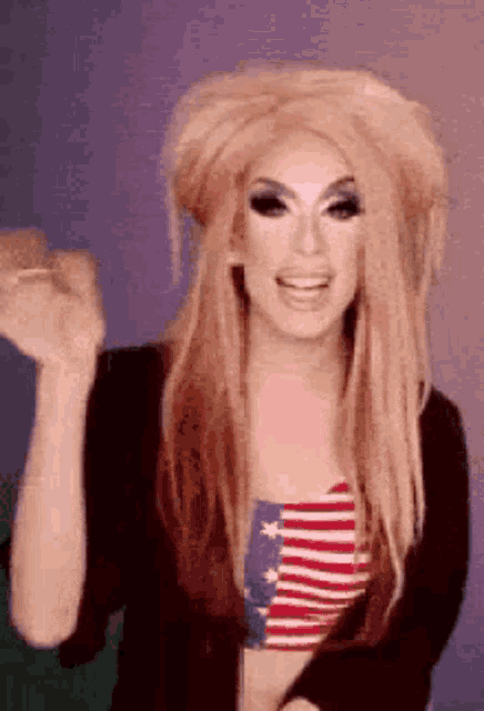 a woman in a wig is wearing an american flag tank top and waving .