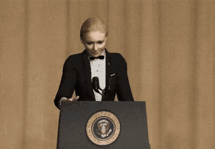 a woman in a tuxedo stands behind a podium with the seal of the president of the united states on it