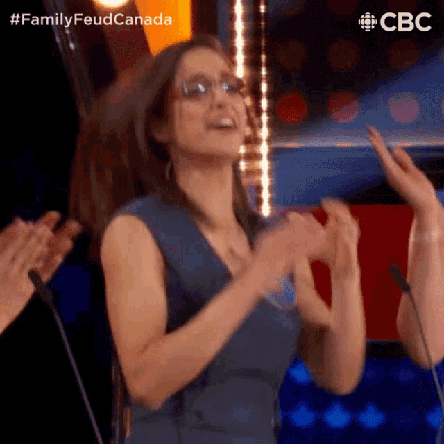 a woman wearing glasses is clapping her hands while standing in front of a microphone on a stage .