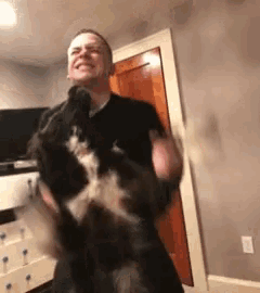 a man is holding a black and white dog in his arms in a room .