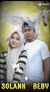a man and a woman are posing for a picture . the man is wearing a unicorn hat .