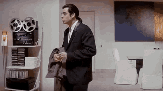a man in a suit and tie is standing in a living room with a tape recorder .