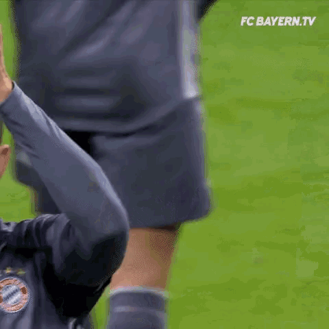 a soccer player is giving a high five to his teammate on a field .