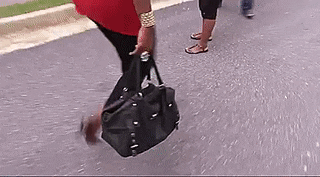 a woman is carrying a black purse while walking down a street .