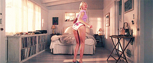 a woman in underwear is dancing in a bedroom with a bed and a table