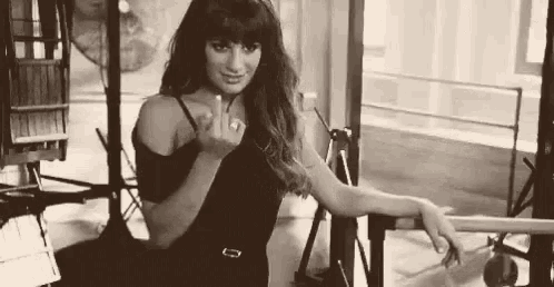 a black and white photo of a woman in a black dress giving the middle finger .