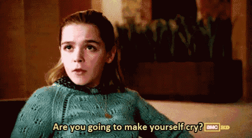 a girl in a blue sweater is sitting on a couch and says are you going to make yourself cry ?