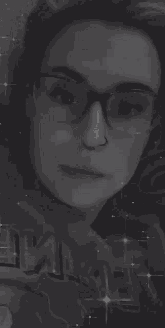 a woman wearing glasses and a nose ring is looking at the camera in a black and white photo .