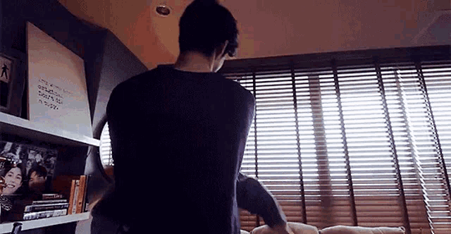 a man is standing in front of a window with blinds in a living room .