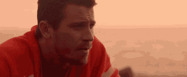 a man wearing a red sweater looks at the ocean
