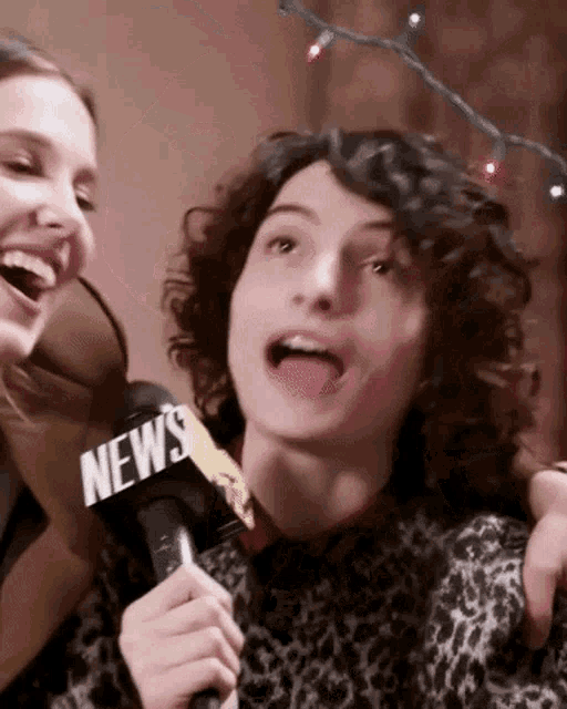 a man and a woman are laughing and holding a microphone that says news .