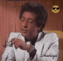 a man in a suit is smoking a cigarette and wearing sunglasses .
