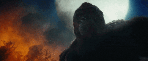 a giant gorilla is standing in front of a full moon in a cloudy sky .