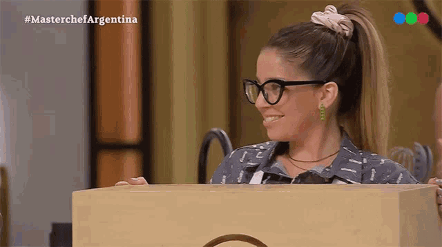 a woman wearing glasses is standing behind a wooden box and smiling
