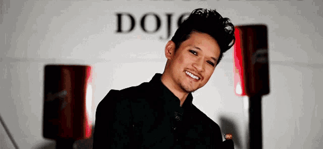 a man in a black shirt is smiling in front of a dojo sign .