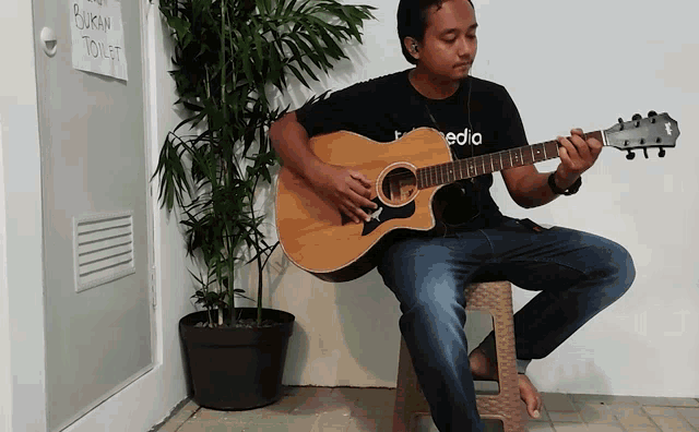 a man sits on a stool playing a guitar in front of a sign that says bukan toilet