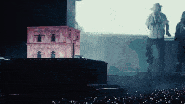 a man stands on a stage holding a microphone in front of a pink building