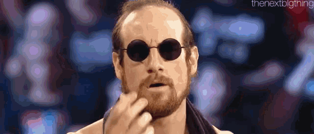 a bearded man wearing sunglasses and a towel around his neck .