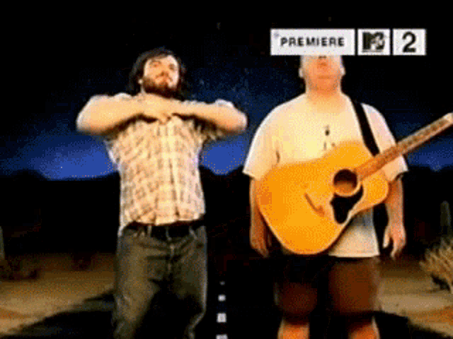 two men standing next to each other with one holding a guitar in front of a sign that says premiere on it