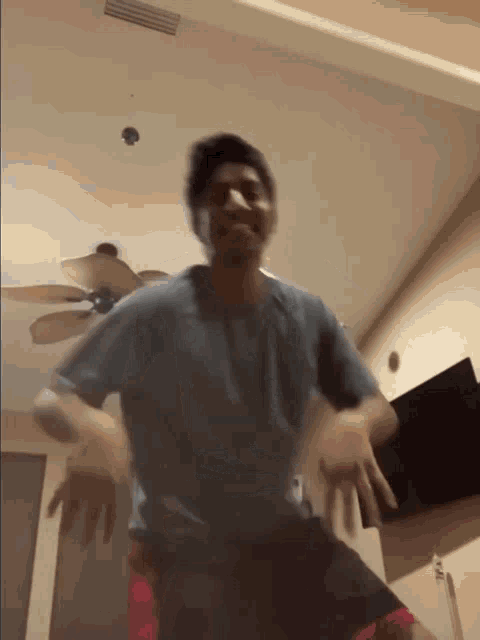a man in a blue shirt and red shorts is dancing in a room with a ceiling fan