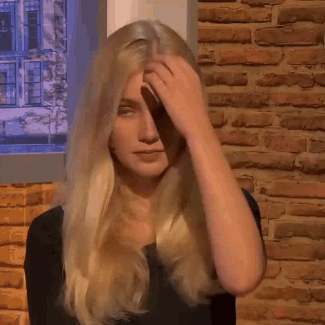 a woman with blonde hair is sitting in front of a brick wall holding her head