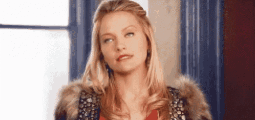 a woman wearing a fur coat and a red shirt is looking at the camera .