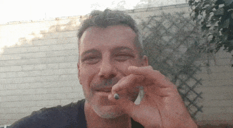a man with a beard is smoking a cigarette and smiling .