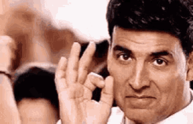 a man in a white shirt is making a funny face while making a peace sign with his hands .