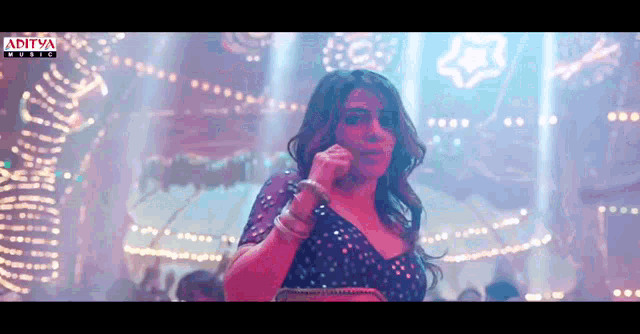 a woman singing into a microphone in front of a sign that says ' aditya music '