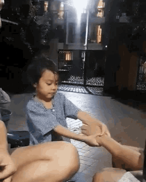 a little boy is holding a woman 's hand while sitting on a brick sidewalk .