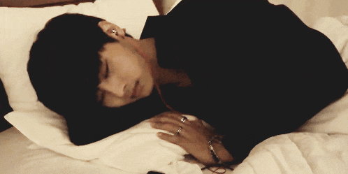 a man in a black shirt is sleeping on a bed with headphones in his ears