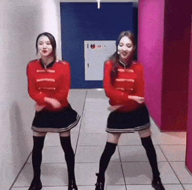 two women are dancing in a hallway with a pink wall