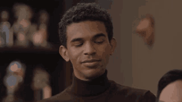 a close up of a man wearing a brown turtleneck sweater smiling .