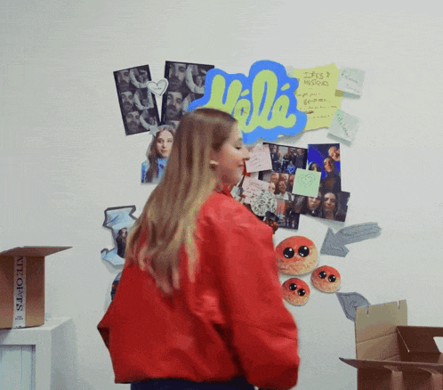 a woman in a red jacket stands in front of a wall with pictures and a sign that says hello