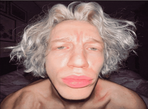 a man with white hair and pink lips is making a sad face