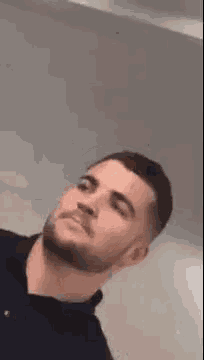 a man with a beard is making a funny face while standing in front of a white wall .