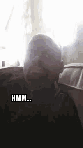 a man with a beard is talking on a cell phone while sitting in front of a window .