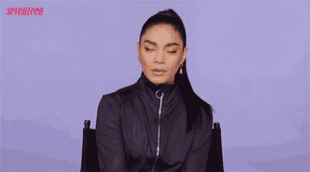 a woman in a black jacket is sitting in a chair with the words whoa written on her shirt .