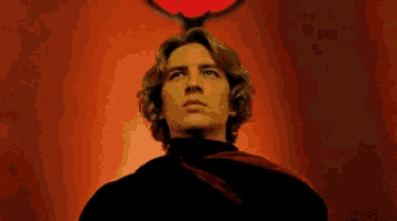 a man with a red scarf around his neck stands in front of a red background